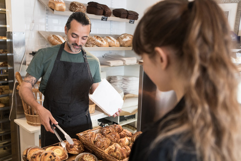 Ein lächelnder reifer Mann serviert einer Kundin in einer Bäckerei frisches Brot, lizenzfreies Stockfoto