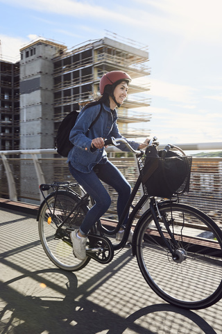 Lächelnde mittelgroße erwachsene Frau, die auf einer Fußgängerbrücke gegen den Himmel radelt, lizenzfreies Stockfoto