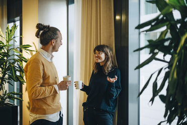 Lächelnde Geschäftsfrau und Geschäftsmann im Gespräch beim Trinken am Fenster im Büro - MASF01197