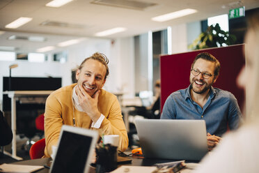 Smiling mid adult male colleagues sitting at conference table while looking away in office - MASF01204