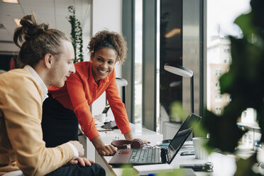 Smiling businesswoman leaning on desk while looking at businessman sitting at office - MASF01207