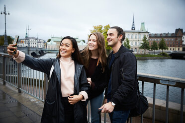 Smiling woman taking selfie through mobile phone while standing on bridge in city - MASF01236