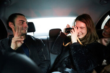 Lächelnde Frau fotografiert männlichen Freund Geste Friedenszeichen während der Fahrt in Taxi in der Stadt - MASF01239