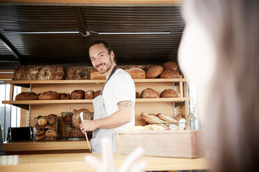 Lächelnder männlicher Besitzer, der frisches Brot in einem Imbissstand verkauft - MASF01251