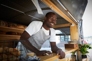 Smiling salesman looking away while standing in food truck - MASF01254