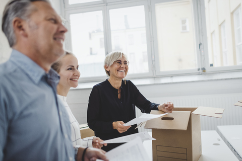 Lächelnder reifer Geschäftsmann mit Kollege beim Auspacken eines Kartons in einem neuen Büro, lizenzfreies Stockfoto