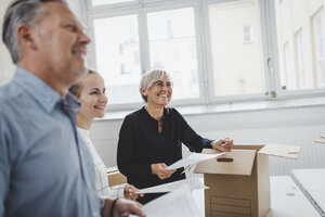 Lächelnder reifer Geschäftsmann mit Kollege beim Auspacken eines Kartons in einem neuen Büro - MASF01257