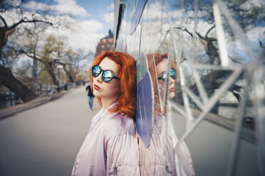 Redhead young woman wearing sunglasses while leaning on mosaic wall by street - MASF01271