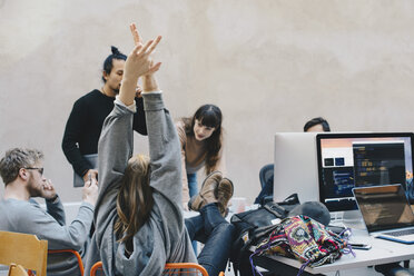 Rückansicht einer Computerprogrammiererin, die ihre Arme ausstreckt, während sie mit Kollegen in einem kreativen Büro sitzt - MASF01276