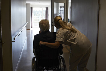 Rückansicht einer Krankenschwester mit einem älteren Mann im Rollstuhl auf dem Krankenhausflur - MASF01277