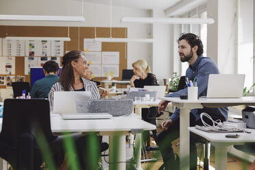 Professionals talking while sitting at desks in creative office - MASF01284