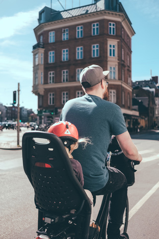 Rückansicht des Vaters auf dem Fahrrad, während die Tochter auf dem Rücksitz in der Stadt sitzt, lizenzfreies Stockfoto