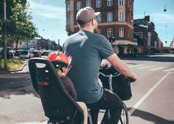 Rear view of father cycling while daughter sitting on back seat at city street - MASF01294