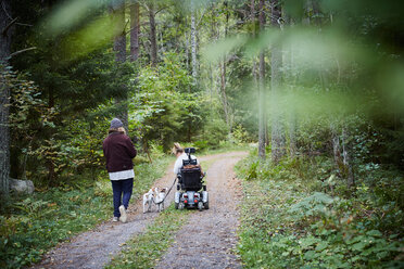 Rückansicht eines jungen männlichen Hausmeisters mit einer behinderten Frau und einem Hund im Wald - MASF01312