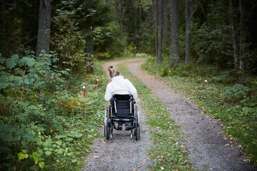 Rückansicht einer behinderten Frau im Rollstuhl auf einem Feldweg im Wald - MASF01314