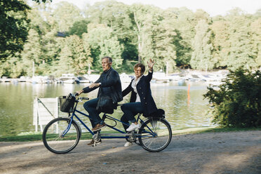 Senior couple enjoying tandem bike ride by pond in park - MASF01331