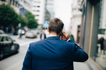 Rear view of mature businessman talking on mobile phone while walking on sidewalk in city - MASF01343