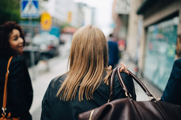 Rückansicht einer Geschäftsfrau, die Gepäck trägt, während sie inmitten von Kollegen auf dem Bürgersteig in der Stadt spazieren geht - MASF01346