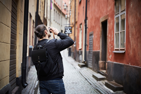 Rückansicht eines Mannes, der durch eine Kamera fotografiert, während er in einer Gasse steht, lizenzfreies Stockfoto