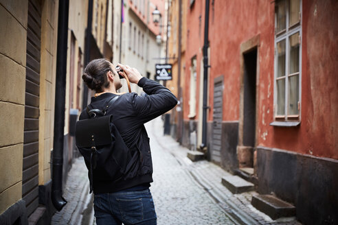 Rückansicht eines Mannes, der durch eine Kamera fotografiert, während er in einer Gasse steht - MASF01349