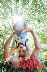 Vater hält Baby kopfüber im Hinterhof liegend - CAVF35182