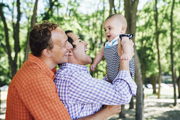 Smiling homosexual couple playing with baby boy at beach - CAVF35187