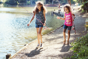 Mädchen tragen Angelruten beim Spaziergang am Seeufer - CAVF35219