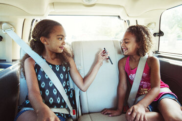 Mädchen zeigt ihrer Schwester während der Fahrt im Auto ihr Smartphone - CAVF35246