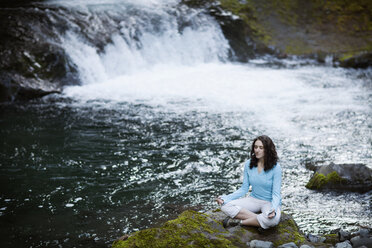 Young woman meditating by stream - CAVF35346