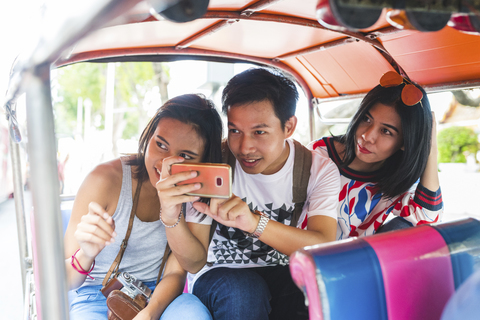 Thailand, Bangkok, drei Freunde fahren Tuk Tuk und fotografieren mit Smartphone, lizenzfreies Stockfoto