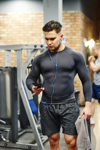 Mann benutzt Mobiltelefon im Fitnessstudio, lizenzfreies Stockfoto