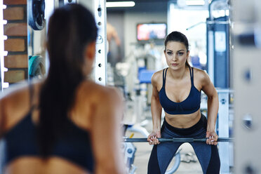 Frau hebt Langhantel im Fitnessstudio und schaut in den Spiegel - ABIF00254