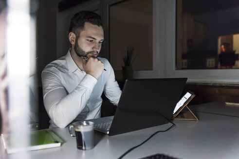 Geschäftsmann bei der Arbeit an einem Laptop im Büro bei Nacht - UUF13195