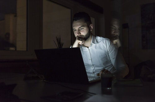 Geschäftsmann bei der Arbeit an einem Laptop im Büro bei Nacht - UUF13196
