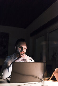 Porträt eines Geschäftsmannes, der nachts im Büro am Schreibtisch sitzt und auf einen Laptop schaut - UUF13197