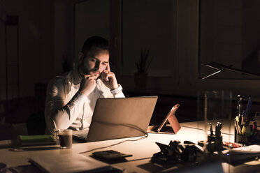 Nachdenklicher Geschäftsmann arbeitet nachts im Büro am Laptop - UUF13198