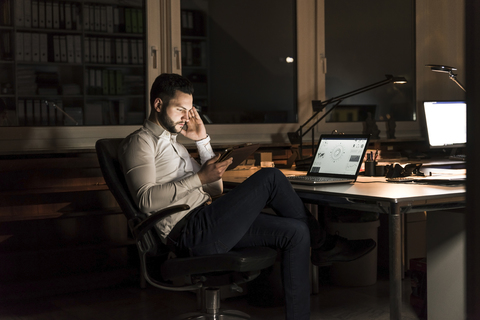 Businessman using tablet in office at night stock photo
