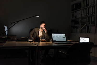 Nachdenklicher Geschäftsmann sitzt nachts am Schreibtisch im Büro - UUF13206