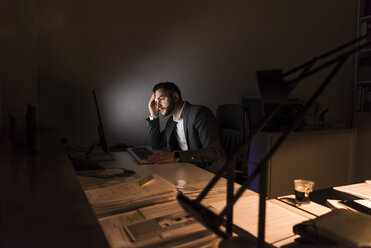 Nachdenklicher junger Geschäftsmann sitzt nachts am Schreibtisch im Büro - UUF13208