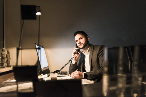 Geschäftsmann am Telefon im Büro bei Nacht, lizenzfreies Stockfoto
