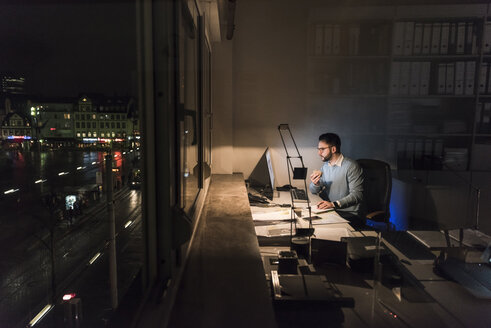 Businessman working on computer in office at night - UUF13212