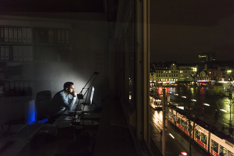 Geschäftsmann bei der Arbeit am Computer im Büro bei Nacht, lizenzfreies Stockfoto
