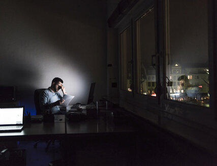 Erschöpfter Geschäftsmann sitzt nachts am Schreibtisch in seinem Büro - UUF13218