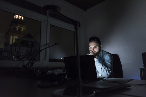 Geschäftsmann bei der Arbeit an einem Laptop im Büro bei Nacht - UUF13219