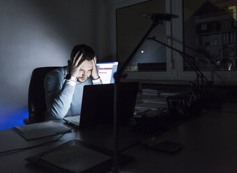 Müder Geschäftsmann sitzt nachts am Schreibtisch im Büro - UUF13220