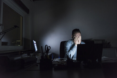 Exhausted businessman sitting at desk in office at night - UUF13221