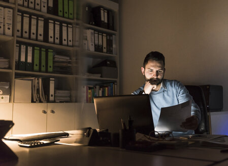 Geschäftsmann arbeitet am Schreibtisch im Büro bei Nacht - UUF13222