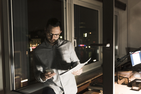 Businessman in office at night using smartphone stock photo