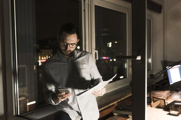 Businessman in office at night using smartphone - UUF13251