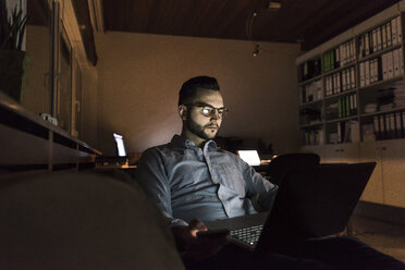 Geschäftsmann bei der Arbeit an einem Laptop im Büro bei Nacht - UUF13252